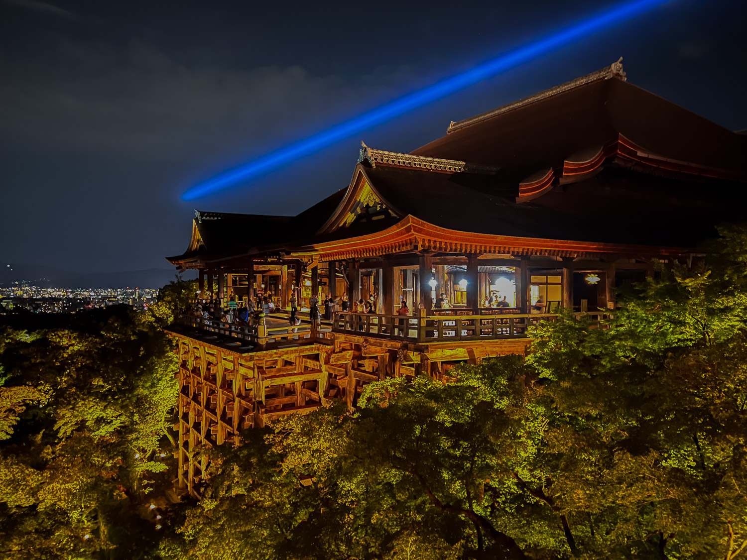 Kiyomizudera's famous wooden stage illuminated at night with the blue beam of Kannon's compassionate light crossing the summer sky during Sennichi-mairi