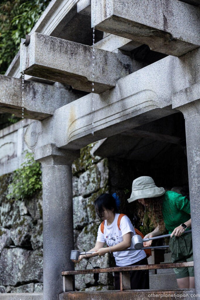 Two visitors drinking from Otowa waterfall at Kiyomizudera using ladles