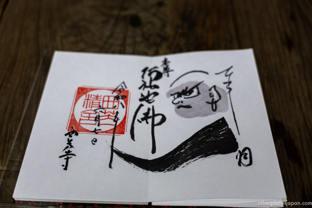 Saihō-ji goshuin stamp with hand-drawn Daruma Daishi ink portrait and Amida Nyorai calligraphy on a wooden table