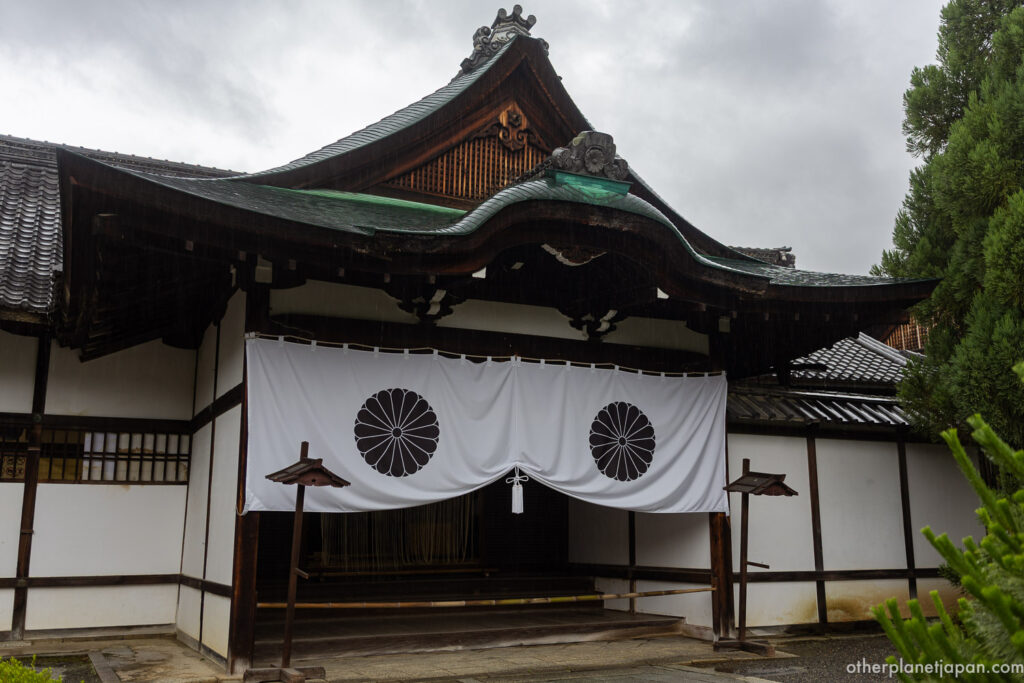 A white curtain bearing the imperial chrysanthemum crest hangs at a temple entrance at Daikakuji in the rain
