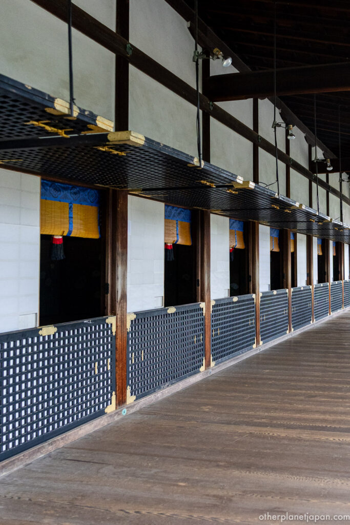 An interior corridor at Daikakuji Temple with lattice panels, golden blinds, and dark wooden flooring stretching into perspective