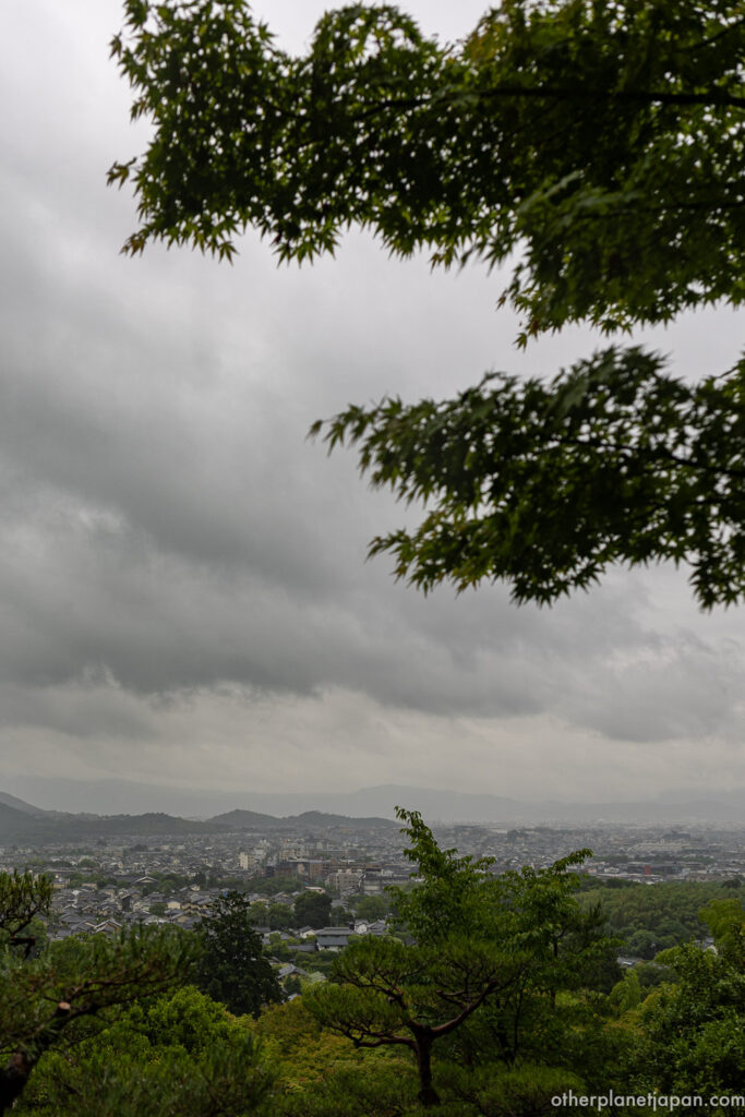  Panoramic view of Kyoto city under cloudy sky framed by maple branches from upper grounds of Jojakkoji