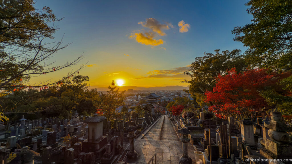 Sunset view over Kyoto from the hilltop cemetery at Konkai-komyoji with stone graves and autumn maples