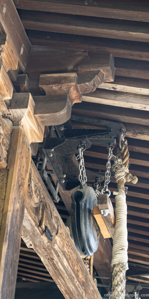 Bronze waniguchi gong and chain hanging beneath wooden eaves of Fudo-do hall at Kinkakuji, Kyoto