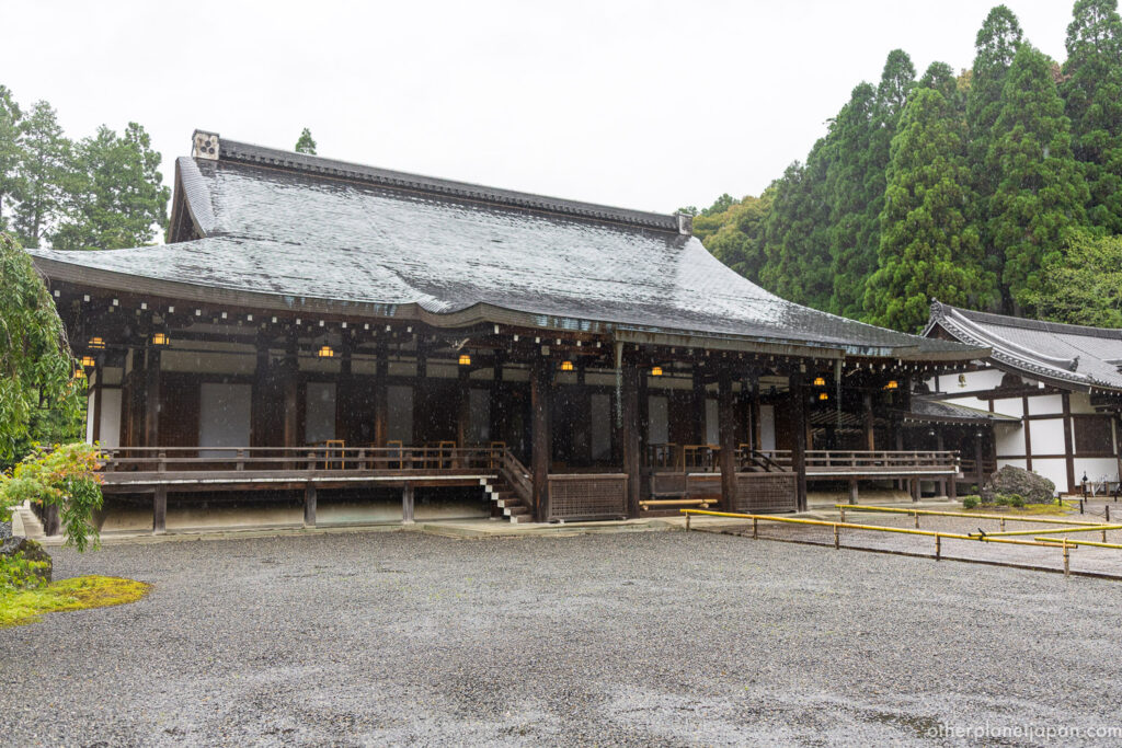 Saihō-ji main hall under heavy rain during Kyoto's tsuyu rainy season, with wet gravel courtyard and cedar trees in the background