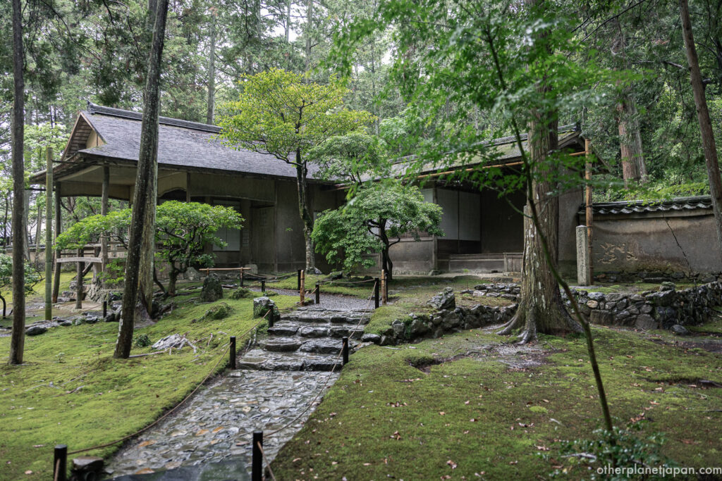 Weathered temple building surrounded by moss, stone paths, and cedar trees inside the Saihō-ji grounds