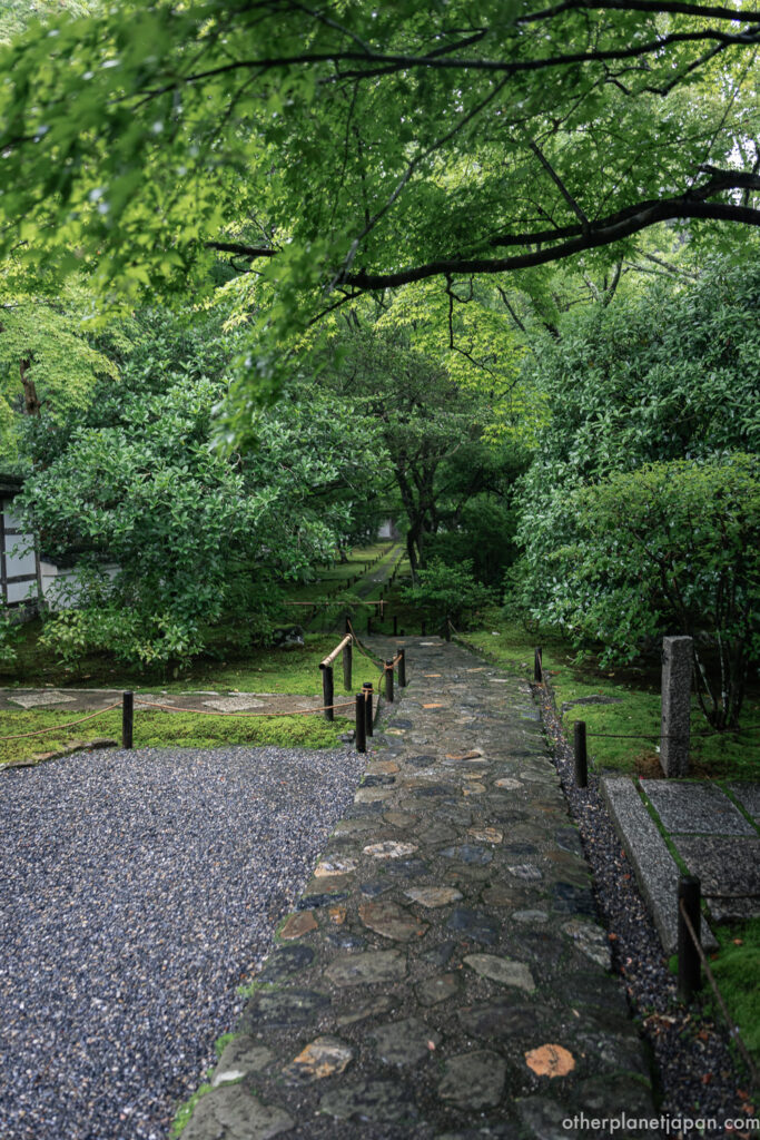 Stone path leading through a corridor of green moss and trees toward an inner gate at Saihō-ji temple in Kyoto