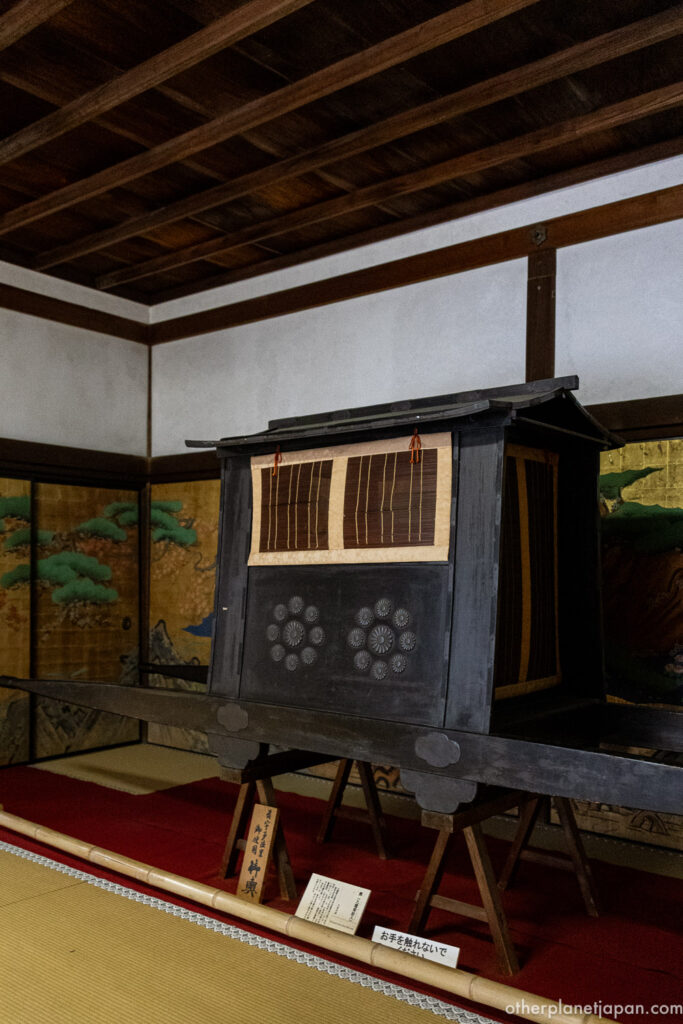 A traditional imperial palanquin displayed on a red carpet with golden folding-screen paintings behind it at Daikakuji Temple in Kyoto