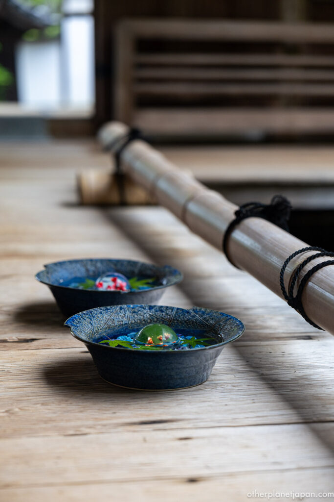 Traditional Japanese ceramic bowls with glass ornaments and maple leaves displayed on a wooden veranda in summer