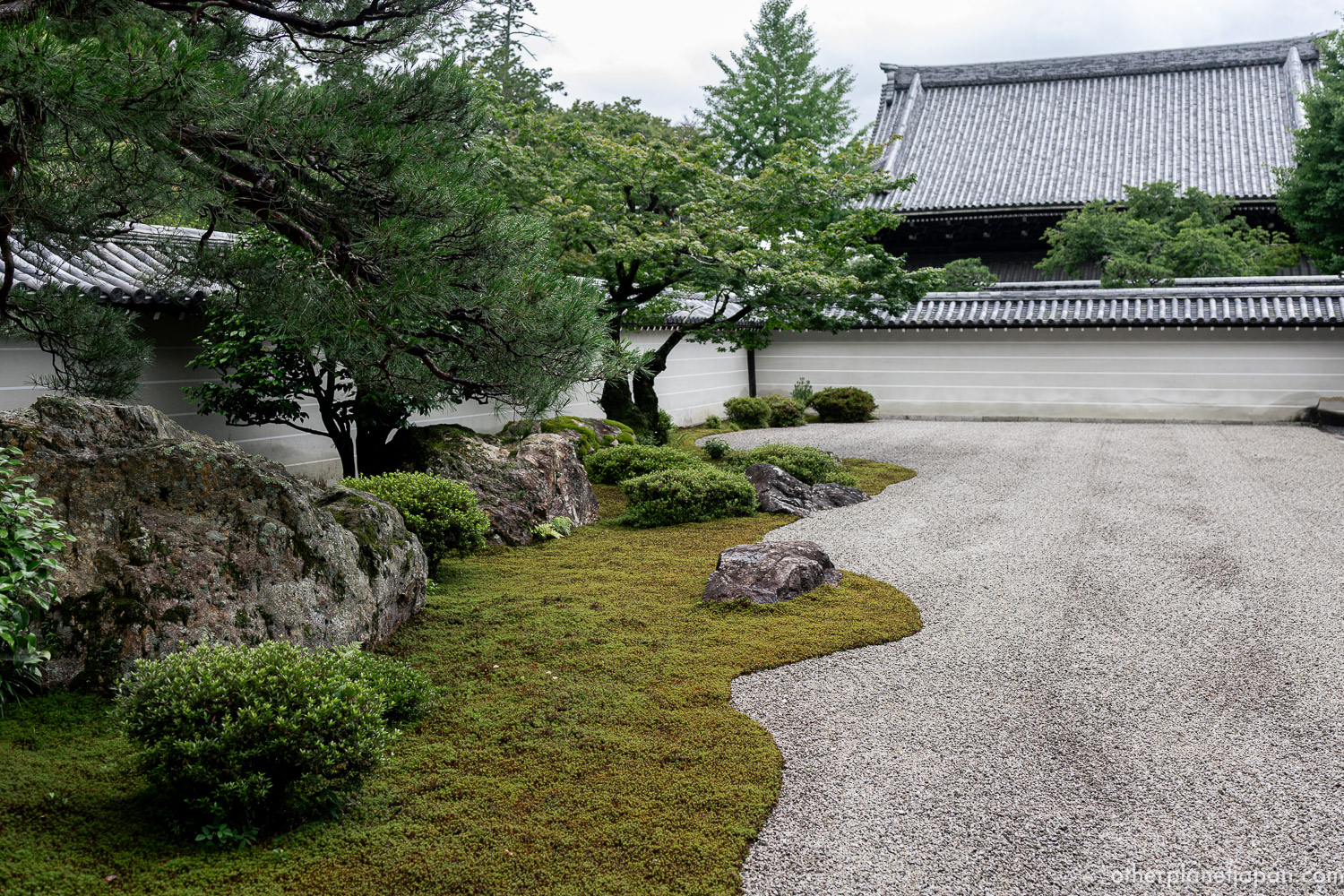 The wide karesansui rock garden of Nanzenji Hojo, with raked white gravel, dark stones, and a pine tree along the back wall in Kyoto.