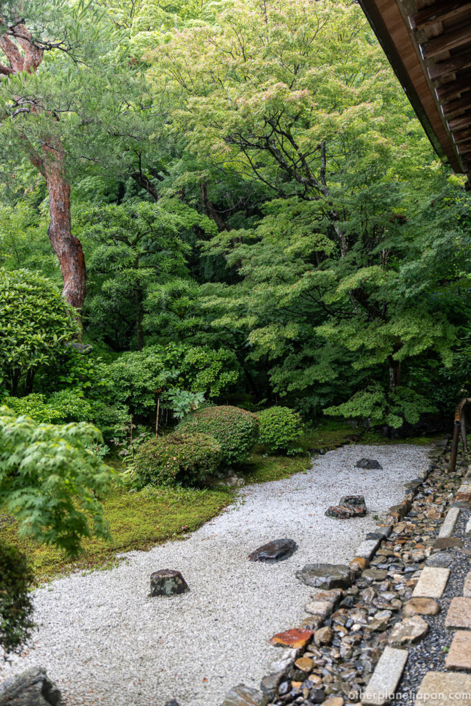 White gravel zen rock garden with scattered stones and lush green foliage at Nison-in Temple
