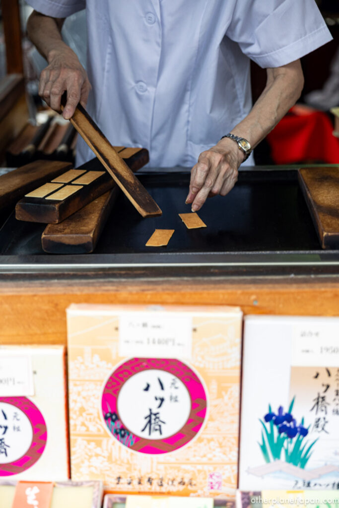 An elderly artisan's hands shaping thin sheets of yatsuhashi sweets on a wooden board near Ginkakuji, Kyoto"