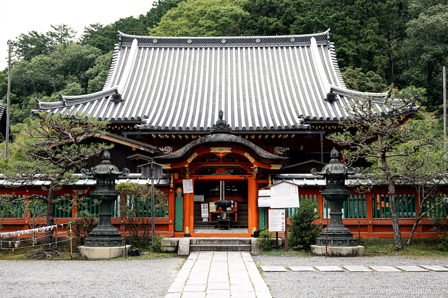 Front view of the vermilion and black main hall of Bishamondo Temple beneath a forested hillside in Kyoto