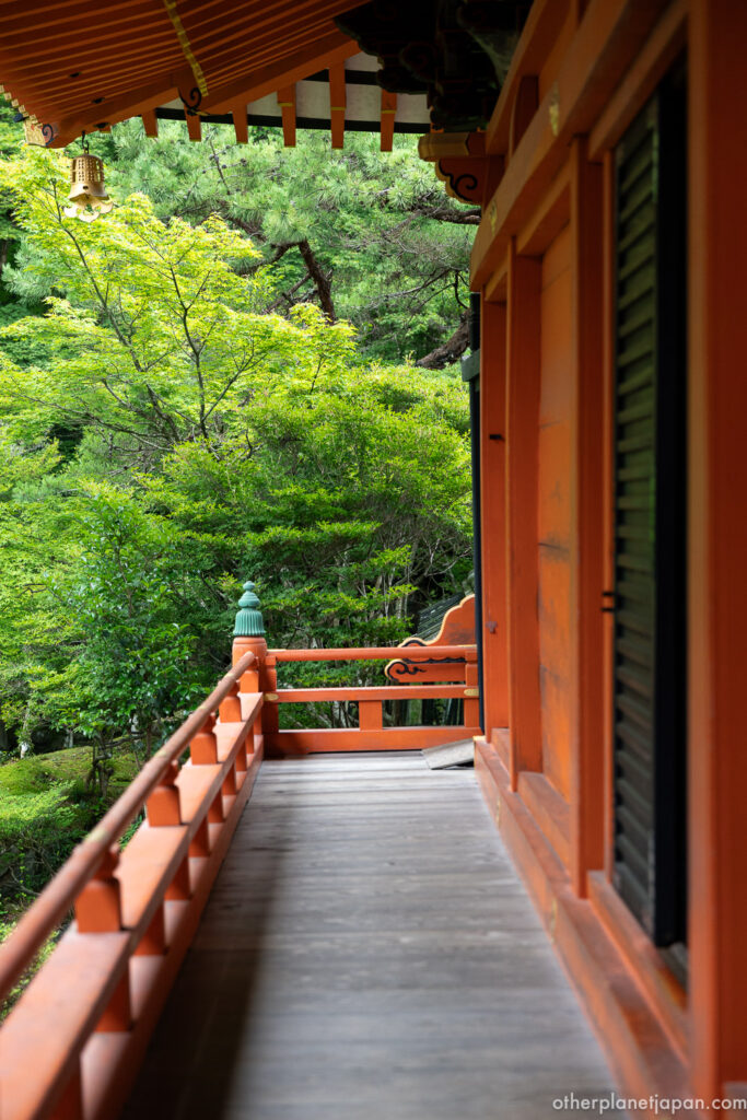 Vermilion wooden veranda of Bishamondo Temple overlooking green maples in Kyoto