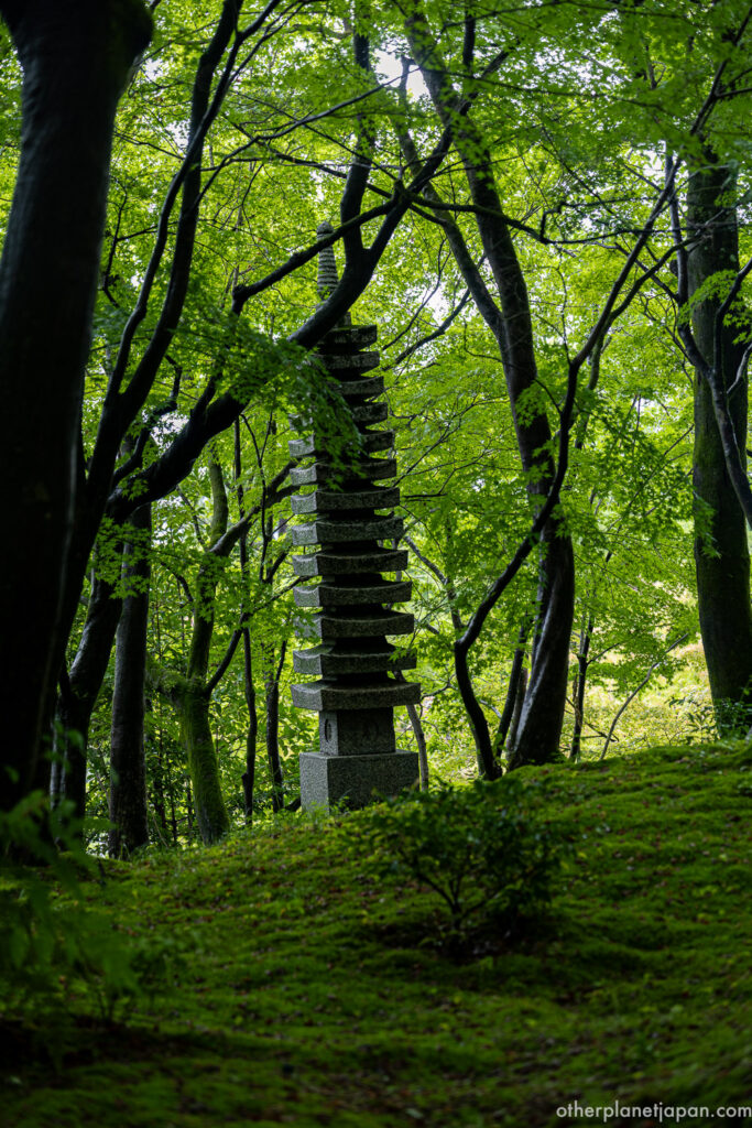 Stone pagoda standing on a mossy slope surrounded by green maple forest at Eikando Temple, Kyoto