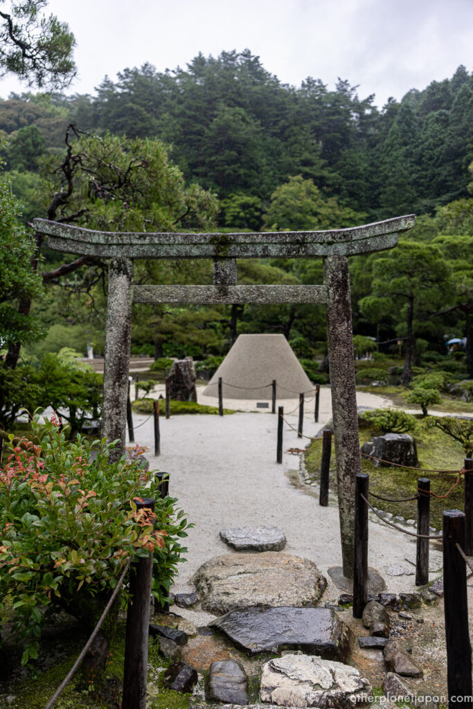 A weathered stone torii gate framing the kogetsudai sand cone along the garden path at Ginkakuji, Kyoto