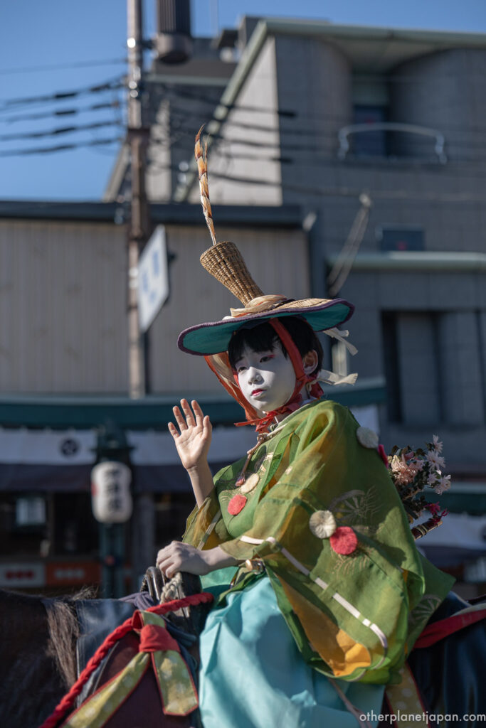 An umaosa chigo boy in ceremonial dress waving from horseback during Gion Matsuri
