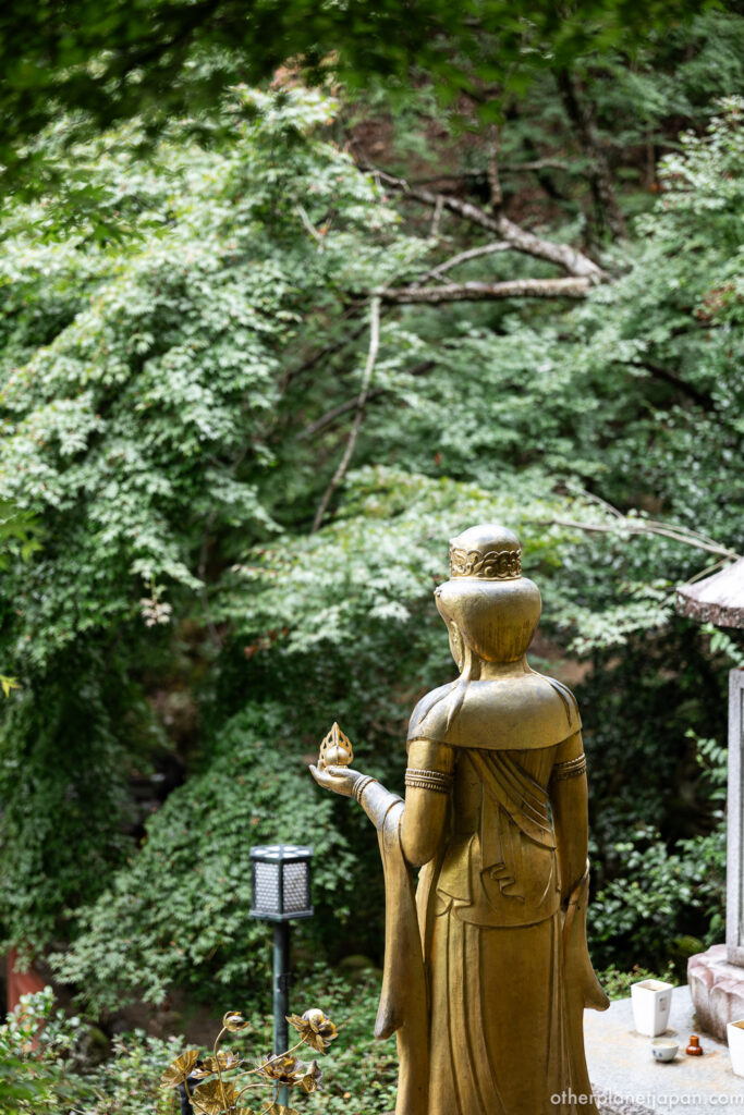 Golden Kannon statue holding a lotus bud overlooking a green valley at Otagi Nenbutsuji, Kyoto
