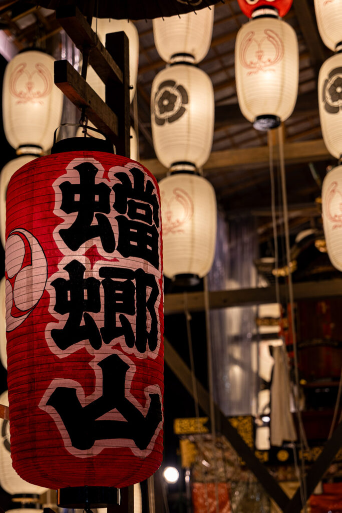 Large red lantern of Toro Yama glowing in front of rows of white paper lanterns at night in Kyoto