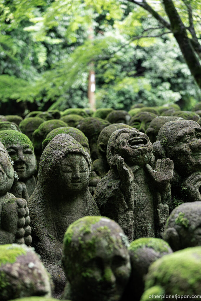 Laughing rakan statue with hands raised among moss-covered stone figures at Otagi Nenbutsuji, Kyoto