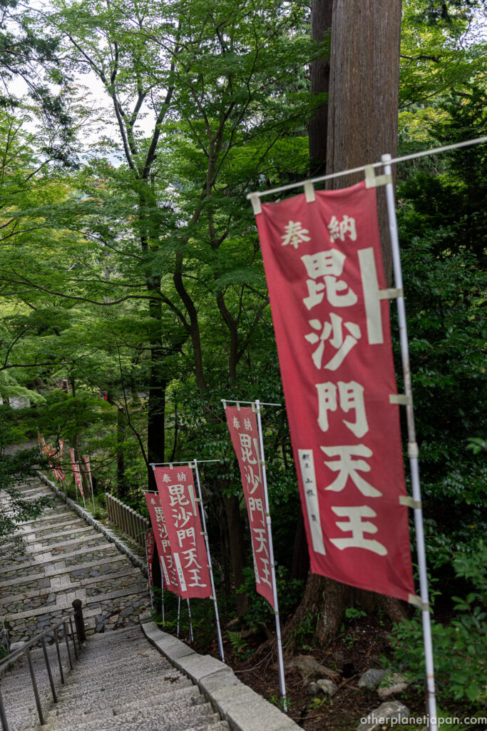 Crimson votive banners for Bishamonten lining a green stone stairway at Bishamondo Temple, Kyoto