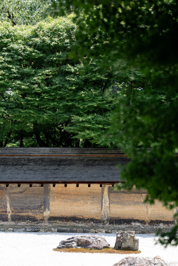 Weathered earthen wall and stones seen through green foliage at Ryoanji rock garden