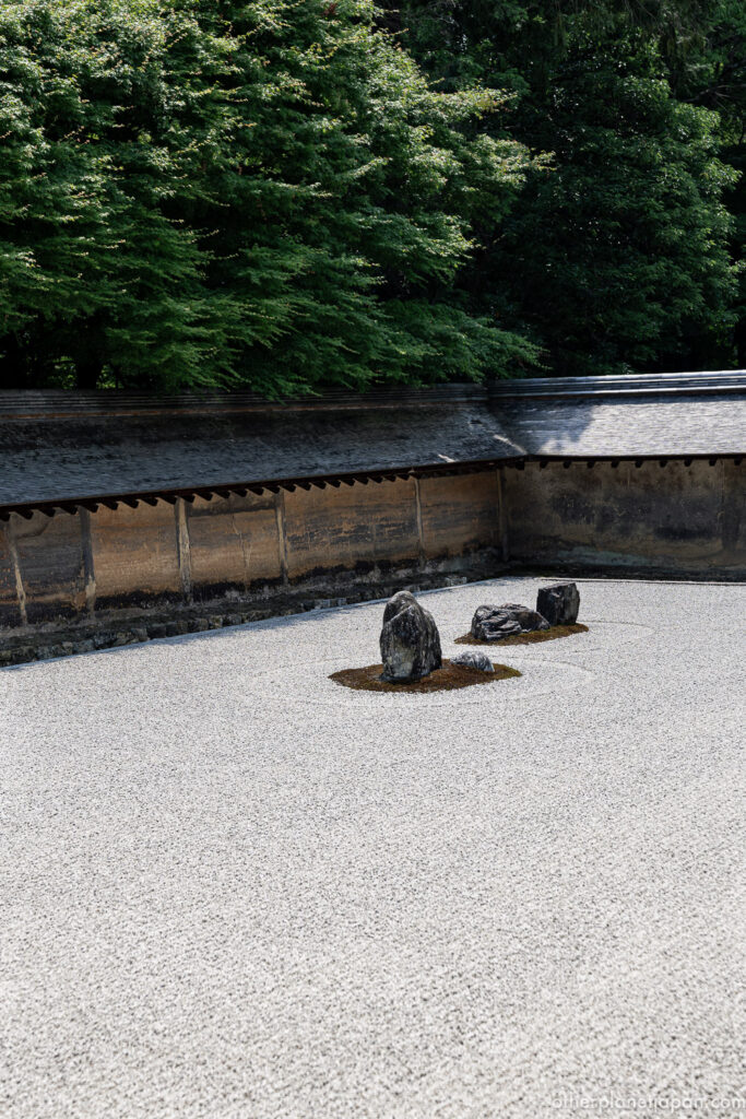 Weathered earthen wall and stones seen through green foliage at Ryoanji rock garden
