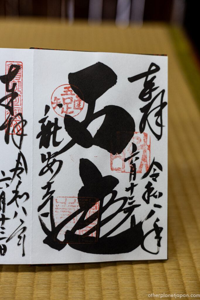 An open goshuin (temple stamp) book resting on a tatami mat. The right page features bold, circular Japanese calligraphy spelling out 'Ware Tada Taru Wo Shiru,' a core Zen philosophy of Ryoan-ji Temple.