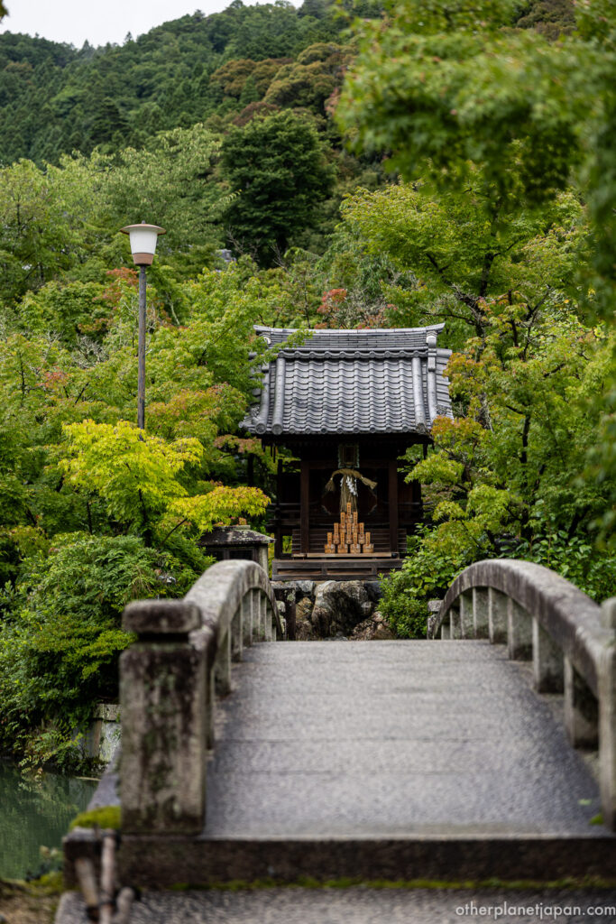 Stone bridge Gokurakubashi leading to a small shrine surrounded by green maples at Eikando Temple, Kyoto
