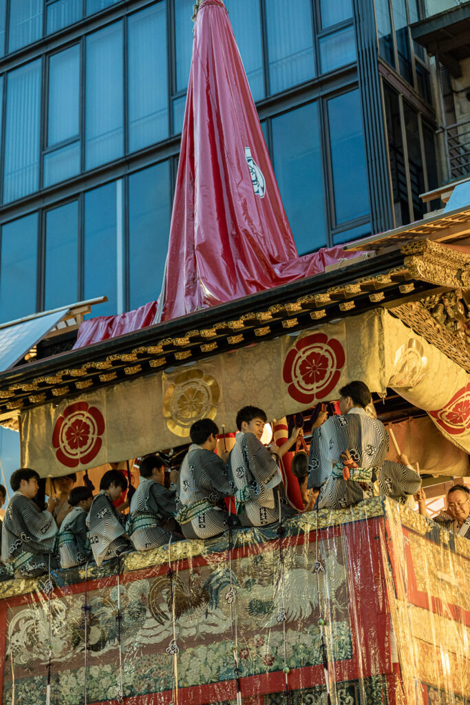 Festival musicians on a gilded Gion Matsuri float in front of a modern glass office building in Kyoto