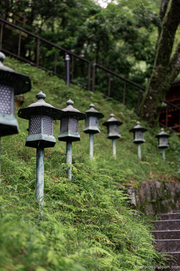 Row of traditional metal lanterns lining a mossy slope beside stone stairs at Otagi Nenbutsuji, Kyoto