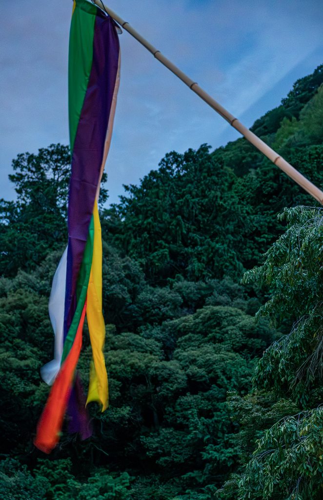  Five-colored Buddhist streamer blowing in the wind against the forested mountains of Arashiyama
