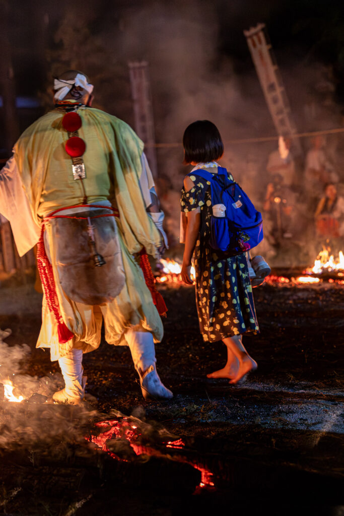 Young child walking barefoot across the fire bed beside a yamabushi monk at the Tanukidani Fudoin fire walking festival