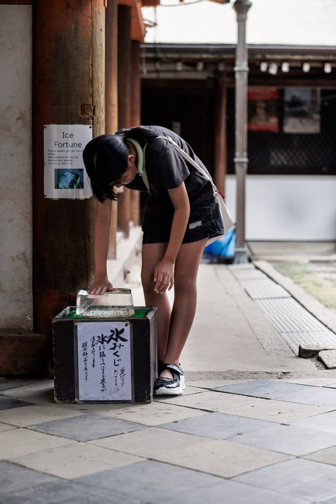 A visitor pressing a fortune slip onto the ice block at Himuro Shrine in Nara