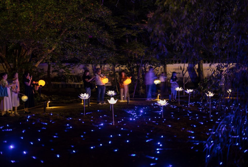 Visitors carrying paper lanterns beside the blue-lit moss garden at the Shoren-in Temple night illumination