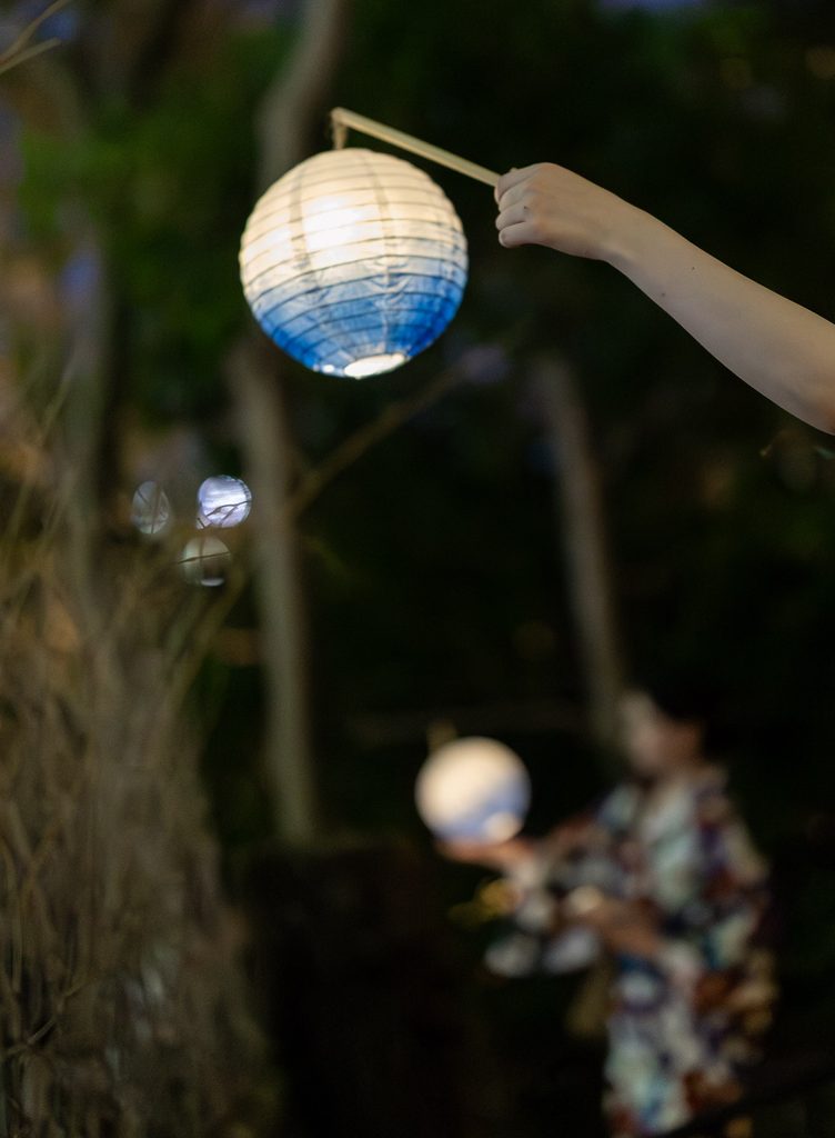 Hand holding a white and indigo paper lantern at Shoren-in Temple, a yukata-clad visitor blurred behind
