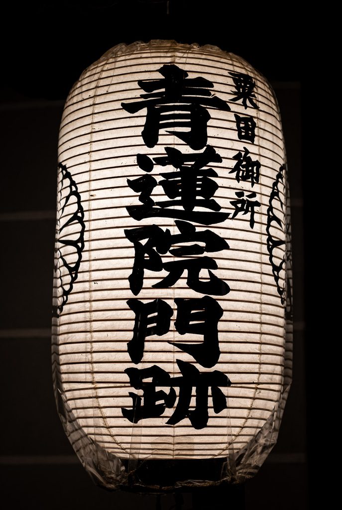 White paper lantern with the name Shoren-in Monzeki written in black calligraphy, glowing against the dark