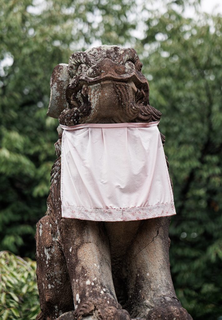 A weathered stone guardian lion at Himuro Shrine wearing a faded cloth bib