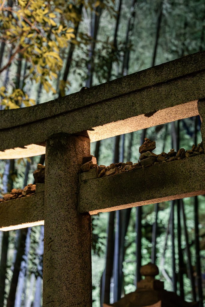 Pebbles resting on the beams of a stone torii gate at the shrine inside Shoren-in Temple, bamboo behind