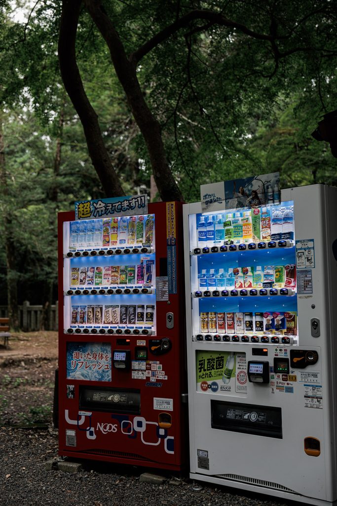 Two brightly lit Japanese vending machines in the forest at Tamukeyama Hachimangu Shrine, Nara