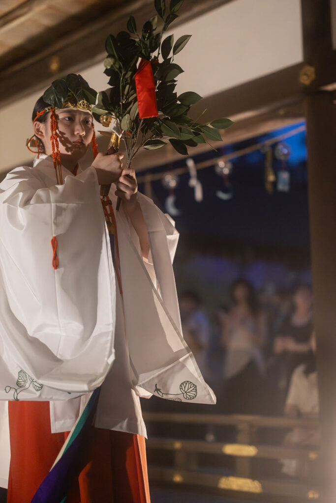 Close-up of a shrine maiden holding a sakaki branch and golden bells during the Kamo-no-Mai dance at Kamigamo Shrine