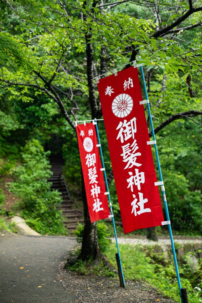 Red banners marking the entrance path to Mikami Shrine in the woods near Ogura Pond