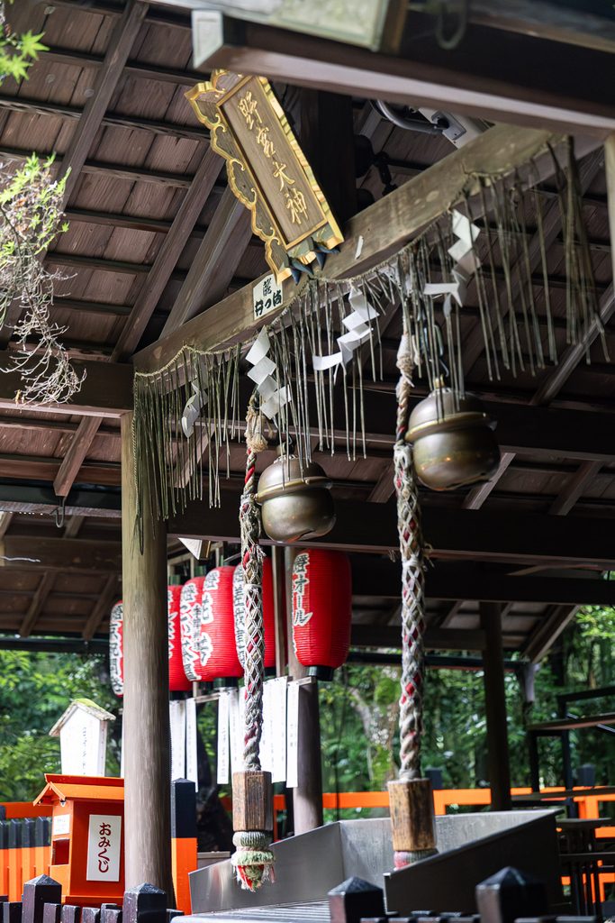 Brass bells and braided ropes hanging under the eaves of the worship hall at Nonomiya Shrine