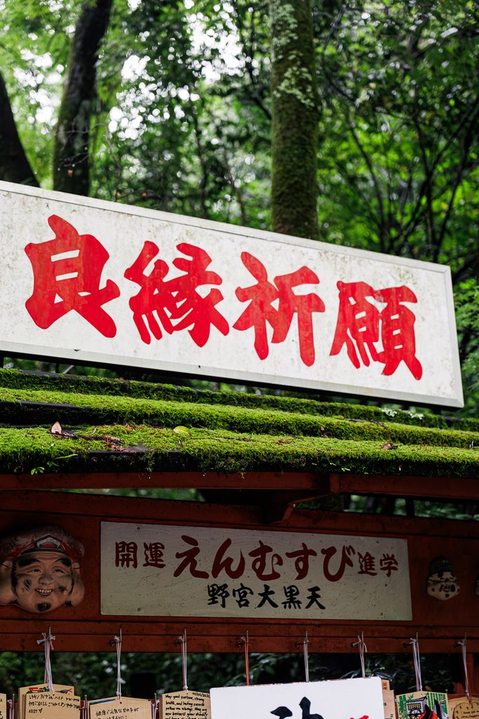 Red calligraphy on a white sign advertising prayers for good relationships at Nonomiya Shrine