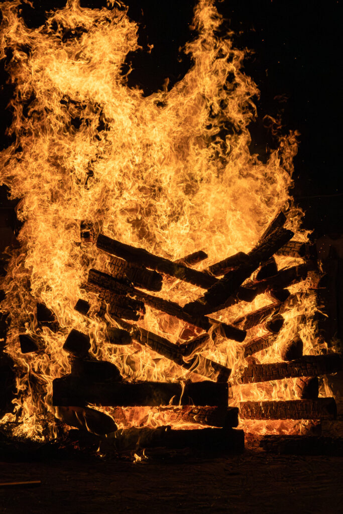 Towering flames of the saito goma fire consuming stacked cedar logs at night during the Tanukidani Fudoin fire walking festival