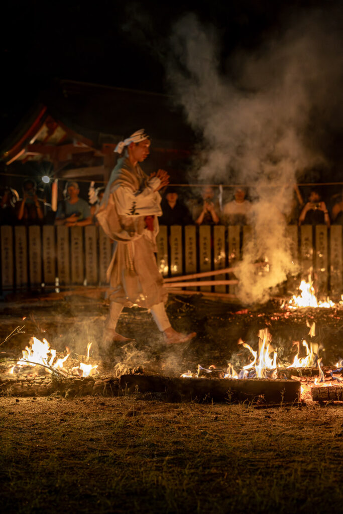 Yamabushi monk walking barefoot across the smoking fire bed with flames burning on both sides at Tanukidani Fudoin