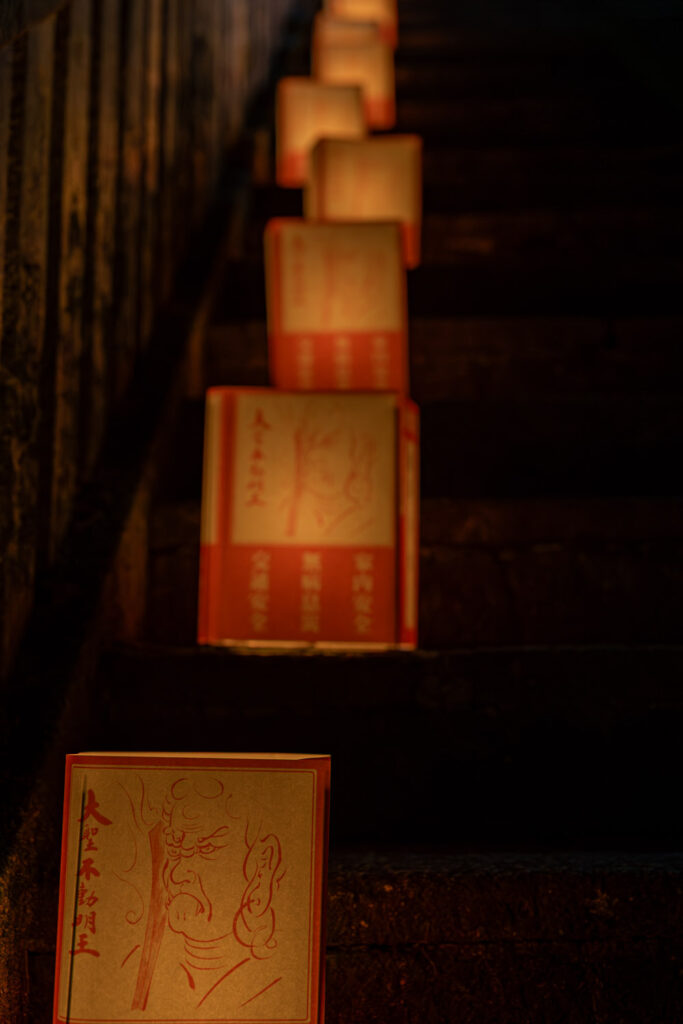 Paper prayer lanterns printed with the face of Fudo Myo-o glowing on a dark stone staircase at Tanukidani Fudoin