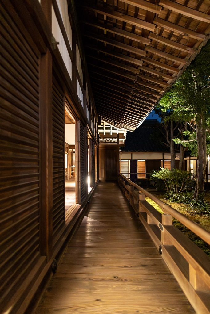 Wooden corridor of Shoren-in Temple lit warm orange at night, with the garden beyond the railing