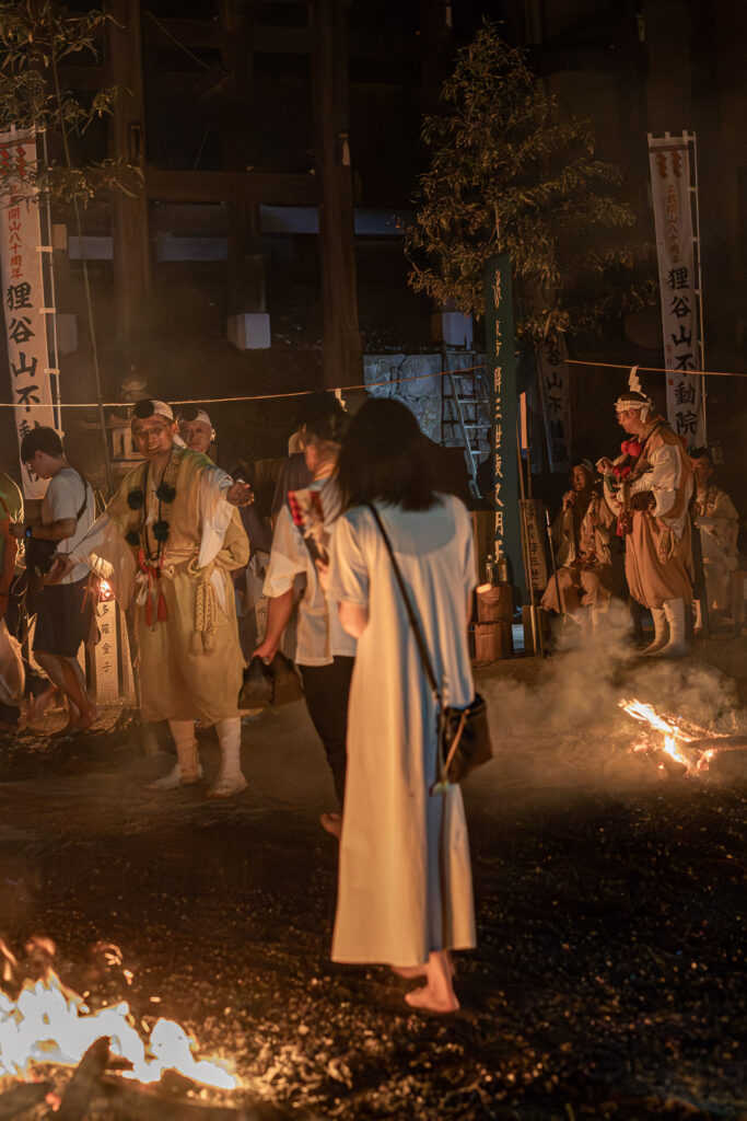 Visitor walking barefoot across the fire bed guided by yamabushi monks as flames burn nearby at Tanukidani Fudoin