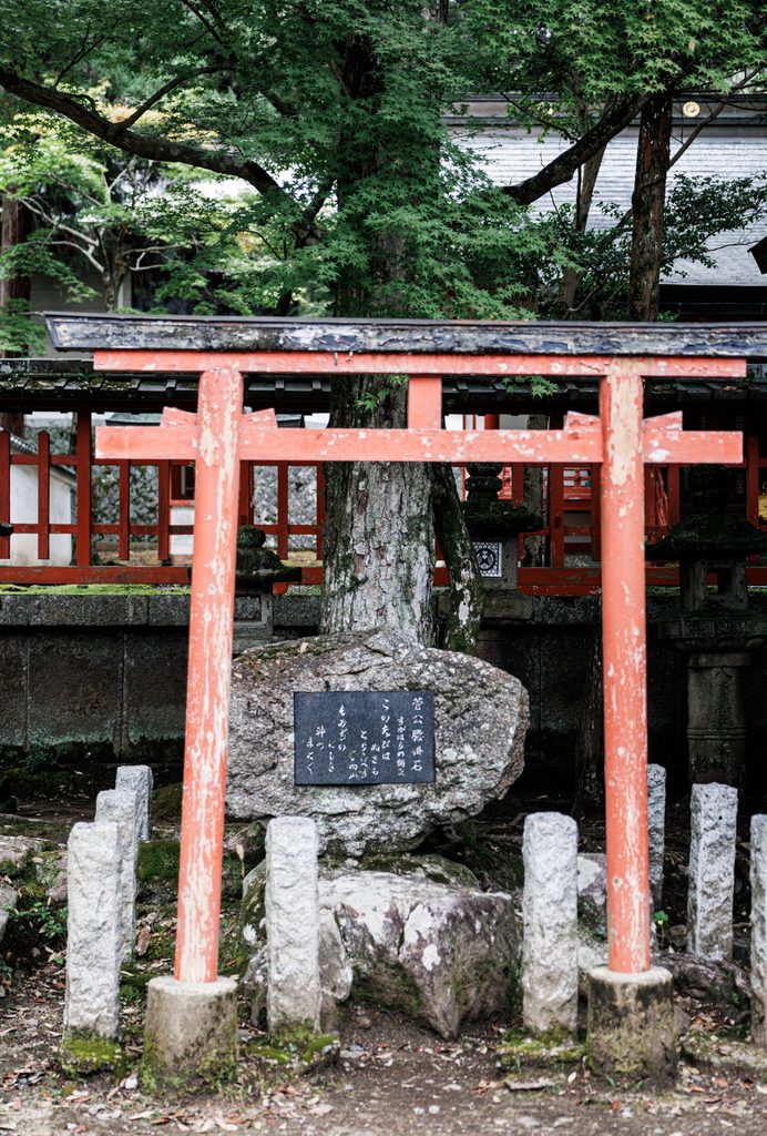 Stone where poet Sugawara no Michizane rested, behind a weathered torii at Tamukeyama Hachimangu Shrine